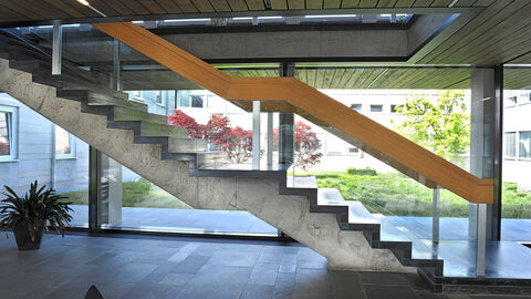 Eine Betontreppe mit Holzgeländer, im Hintergrund eine Fensterfront
