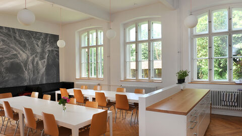 Blick in die alte Schule Vasbeck; ein ehemaliges Klassenzimmer wurde zum hellen Esszimmer mit Holzboden, weißen Tischen und Holzstühlen umgestaltet