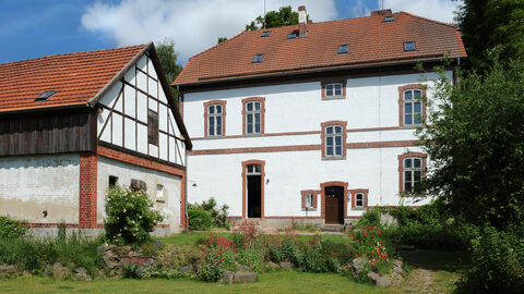 Die Alte Schule Vasbeck von außen, ein weißes Haus mit Nebengebäude und rotem Dach