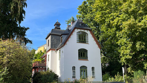 Die Villa Stosch von außen, eine weißverputzte Villa mit grauem Dach und Türmchen