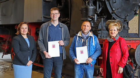 Staatssekretärin Ayse Asar steht mit Mitgliedern des Vereins Museumeisenbahn Hanau vor einer historischen Lokomotive