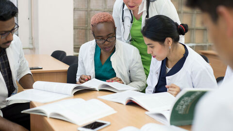 Eine Gruppe Menschen in weißen Kitteln sitzt an einem Tisch und schaut in Medizinbücher