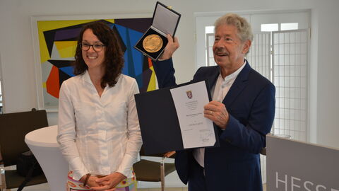 Ministerin Dorn steht neben dem Musiker Reimer von Essen, er hält begeistert die Auszeichnung in die Luft, sie lächelt