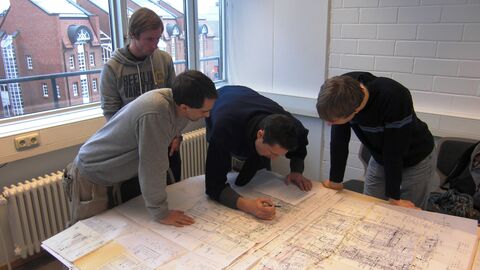 Beim Projekt Solarcampus arbeiten Masterstudierende des Maschinenbaus und der Wirtschaftswissenschaften wie in einem Ingenieurbüro daran, die Energieeffizienz von Gebäuden und Betrieben zu verbessern. Studierende beugen sich über architektonische Pläne.