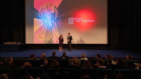 Kinosaal in Kassel, auf der Leinwand steht das Filmpreislogo, auf der Bühne davor steht Staatssekretärin Ayse Asar