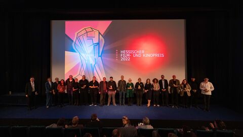 Kinosaal in Kassel, vor der Leinwand stehen die Preisträgerinnen und Preisträger des zweiten Verleihungsabends des Hessischen Film- und Kinopreises 2022