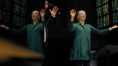 In banda vocale haben die Studierenden die Möglichkeit, mit einem Ensemble aus professionellen Sängerinnen und Sängern zu arbeiten. Eine junge Frau hebt die Arme zur Dirigentenpose vor einem Chor.