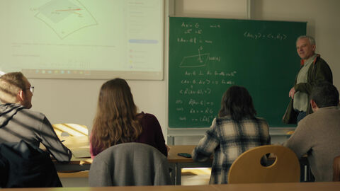 Der mit 60.000 Euro dotierte 1. Projektpreis geht 2022 an Prof. Dr. Karlheinz Spindler für sein Projekt „Holistische Lehre und forschendes Lernen in der Mathematik“ an der Hochschule RheinMain. Szene aus dem Film zum „Holistische Lehre und forschendes Lernen in der Mathematik“: Man sieht Prof. Spindler an der Tafel und Studierende