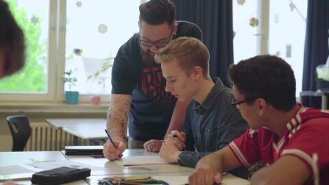 Ein Lehrer zeigt Schülern etwas in ihrem Heft.