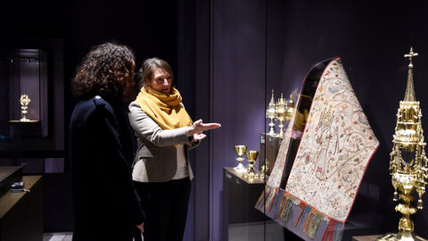 Zu den Ausstellungsstücken zählen auch Textilien. Ministerin Dorn schaut sich ein Ausstellungsstück an.