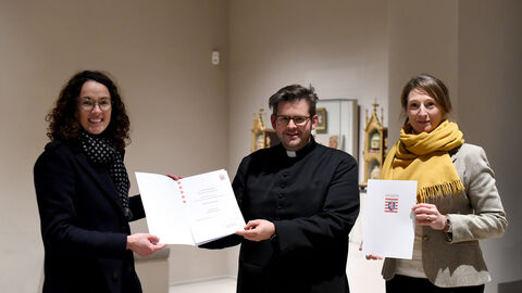 Ministerin Dorn übergibt Stadtpfarrer Patrick Prähler und Kuratorin Stefanie Cossalter-Dallmann die Auszeichnung.