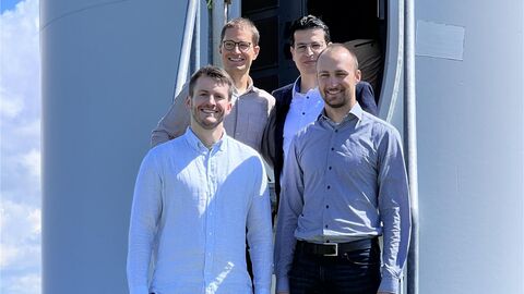 Das Team von Hopes, Pascal Koschwitz, Falah Alobaid, Victor Breburda und Lukas Kaiser von der TU Darmstadt, stehen auf einem Feld mit Windrädern