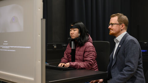 Im Labor von Professor Wallis werden hochpräzise Display- und Eye-Tracking-Systeme eingesetzt, um Experimente zum menschlichen Verhalten durchzuführen.  TU-Professor Thomas Wallis sitzt mit einer Probandin vor einem Bildschirm. Die Probandin ist an ein Messgerät angeschlossen.