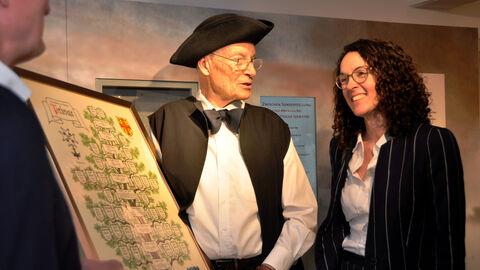 Ein Mann im Kostüm mit Dreispitz und Fliege zeigt Ministerin Dorn eine Ahnentafel.