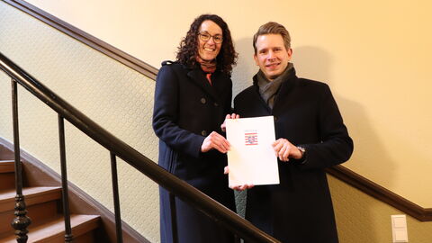 Angela Dorn und Eigentümer Andreas Seydelmann stehen auf einer Treppe im renovierten Haus in der Gutleutstraße und halten die Auszeichnung zum "Denkmal des Monats" in den Händen