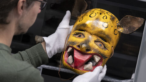 Blick ins Depot eines Museums (Symbolbild). Eine Person hält mit Handschuhen eine indigene Maske.
