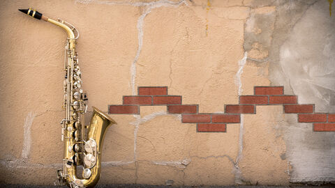 Ein Saxophon ist an eine Wand gelehnt. Ziegelsteine sind so platziert, dass sie aussehen wie eine Melodie, die aus dem Saxophon kommt.