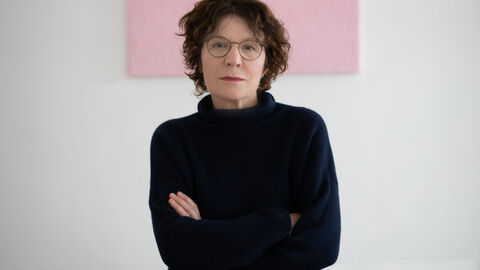 Porträt von Katrin Brack, eine Frau mit kurzen dunklen Haaren. Sie hat die Arme verschränkt und schaut ernst.