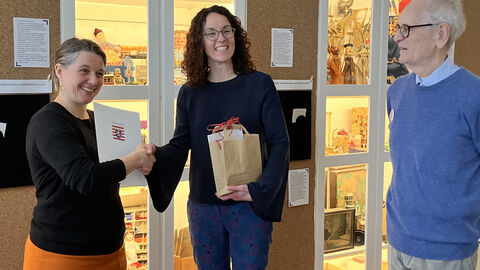 Ministerin Dorn steht mit einer Vertreterin und einem Vertreter des Hessischen Puppen- und Spielzeugmuseums vor einer Vitrine und überreicht die Auszeichnung.