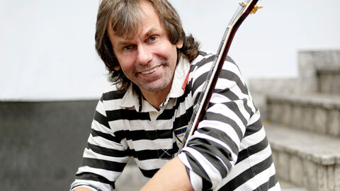 Michael Sagmeister hat 2019 den Hessischen Jazzpreis erhalten. Porträt von Michael Sagmeister, er sitzt auf einer Treppe und hält eine Gitarre in den Händen.