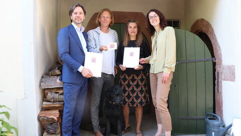 Dr. Marcus Gwechenberger (Planungsdezernat), die Eigentümer Jonas Dreß und Marta Leszczynska mit Ministerin Angela Dorn. Dr. Marcus Gwechenberger (Planungsdezernat), die Eigentümer Jonas Dreß und Marta Leszczynska und Ministerin Angela Dorn stehen vor dem Haus und zeigen die Urkunde.