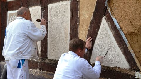 Die Tradition des hessischen Kratzputzes geht bis ins 17. Jahrhundert zurück. Handwerker beim Kratzputzen: Sie ritzen mit spitzen Werkzeugen Ornamente in den weichen Putz einer Fachwerkhauswand