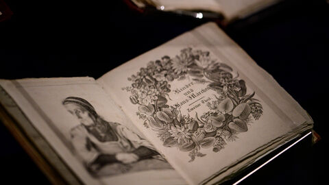 2005 nahm die UNESCO die Handexemplare der Hausmärchen in das Weltdokumentenerbe auf.  Aufgeschlagenes Handexemplar der Grimm’schen Märchen: Auf einer Sei-te ist das handgezeichnete Porträt einer alten Frau zu sehen, rechts der prunkvoll verzierte Buchtitel