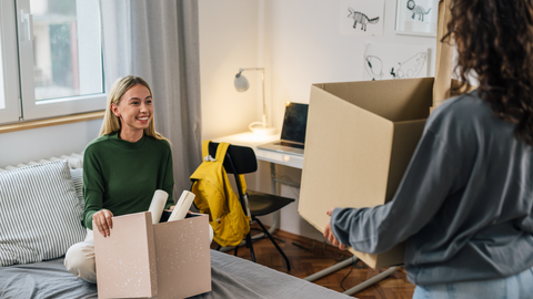 Studierendenwohnheim Zwei Frauen mit Umzugskartons in den Händen, die ein Zimmer beziehen