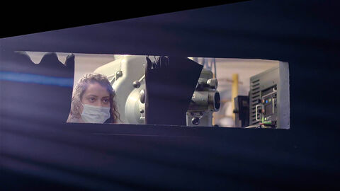 Szene aus "Das Kino sind wir" Szene aus "Das Kino sind wir": eine Frau mit Atemschutzmaskeb steht während der Pandemie neben einem Kinofilmprojektor.