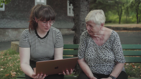Szene aus "Von dem, was bleibt" Szene aus "Von dem, was bleibt": Die Regisseurin Johanna Groß sitzt neben einer alten Frau auf einer Bank und zeigt ihr etwas in einem Laptop.