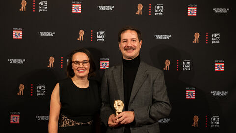Emiliano Proietti, Gewinner in der Kategorie "Bester Hochschulabschlussfilm", und Hessenfilm-Chefin Anna Schoeppe vor der Fotowand
