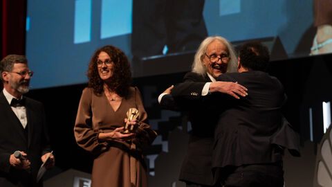 Ministerin Dorn, Laudator und Preisträger auf der Bühne, sie umarmen sich