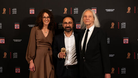 Kunst- und Kulturministerin Angela Dorn mit Newcomer-Preisträger Behrooz Karamizade (Mitte) und Laudator Thomas Mauch vor der Fotowand