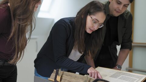 Die Studierenden arbeiten an internationalen Forschungsinstitutionen in Florenz und üben dort den Umgang mit Originalquellen. Studierende beugen sich über ein historisches Buch.