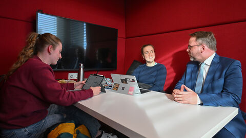 Auf der Lernebene im Obergeschoss bieten Einzelarbeitstische, Gruppentische und Arbeitsboxen vielseitige Möglichkeiten für konzentriertes Lernen und Arbeiten. Minister Gremmels sitzt mit Studierenden in einer roten Lernbox.
