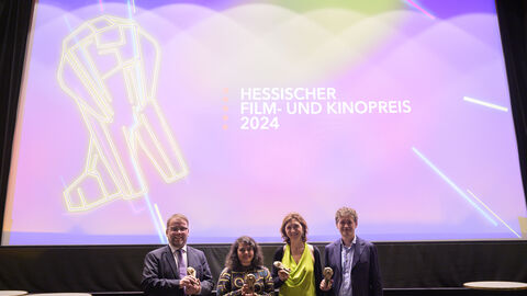 Kunst- und Kulturminister Timon Gremmels hat die ersten Ausgezeichneten und Nominierten des Hessischen Film- und Kinopreises vorgestellt. Minister Gremmels vor einer großen Leinwand mit dem Logo des Hessischen Film- und Kinopreises.
