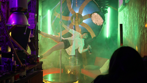 Szene aus "It’s (Not) A Men’s World" Szene aus "It’s (Not) A Men’s World": Eine Frau hängt an einer Poledancestange, bekleidet, mit einer Bierflasche in der Hand