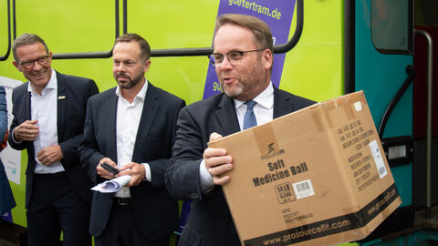 Am Hessischen Tag der Nachhaltigkeit hat Wissenschaftsminister Timon Gremmels das Forschungsprojekt „LastMileTram RheinMain V“ in Frankfurt besucht Minister Gremmels trägt ein Paket.