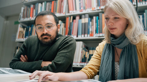 Mehr Qualität in Studium und Lehre - hessenweit. Zwei Studierende sitzen in einer Bibliothek über ihren Büchern.