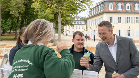 Beim Aktionstag "Wissen wächst im Garten" lernten die Besucherinnen und Besucher den Staatspark Hanau-Wilhelmsbad als Gartenkunstwerk kennen. Staatssekretär Degen liest eine Karte an einem Aktionsstand.