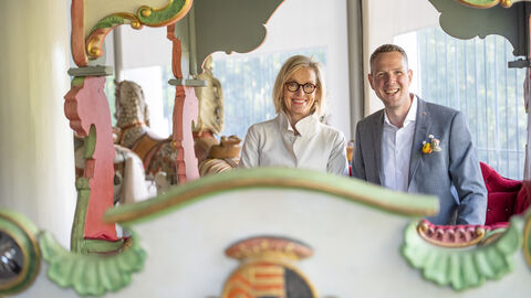 Staatssekretär Christoph Degen und Kirsten Worms, Leitern der Schlösser und Gärten Hessen, sitzen in einer Kutsche auf dem antiken Karussell im Staatspark