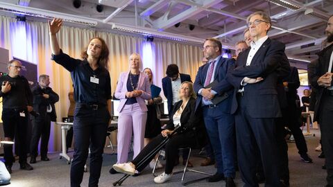 Mehrere Menschen schauen gespannt in eine Richtung und hören einer Frau beim Sprechen zu.