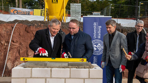 Grundsteinlegung für das  „Marburg Centre for Epidemic Preparedness“ (MCEP) Zwei Männer schauen auf eine Wasserwaage und prüfen, ob alles gerade ist-