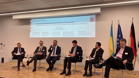 EU-Strategietagung der Hochschulrektorenkonferenz in Brüssel  Mehrere Männer sitzen auf einer Bühne auf einem Stuhl