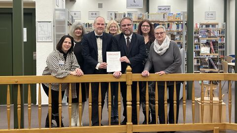 Minister Gremmels steht mit dem Team der Stadtbücherei Korbach hinter einem hölzernen Treppengeländer und überreicht die Urkunde für den Hessischen Leseförderpreis.