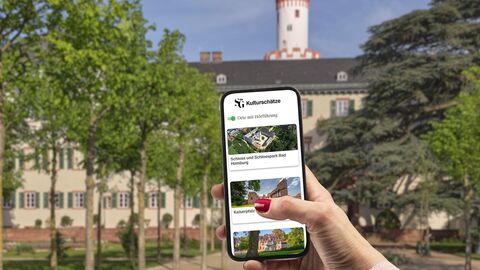 Eine Hand hält ein Handy mit der SG-App vor den Adolfsturm in Bad Homburg.