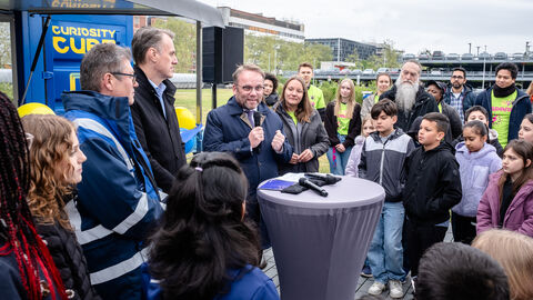 Minister Gremmels hat bei Merck in Darmstadt den Startschuss für die diesjährige internationale Curiosity-Cube-Tour gegeben Minister Gremmels hält eine Rede, umringt von Kindern.