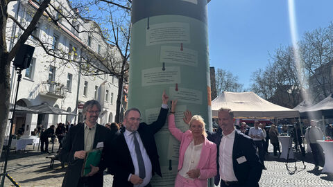 Minister Gremmels zeigt auf die Litfaßsäule.