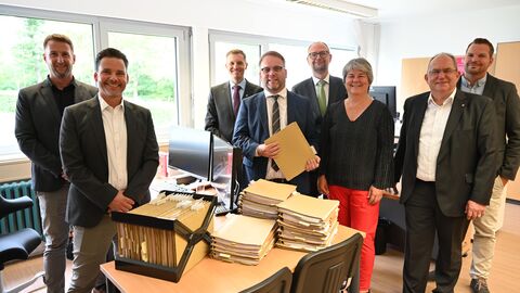 Minister Gremmels steht mit weiteren Menschen vor einem Stapel Akten.