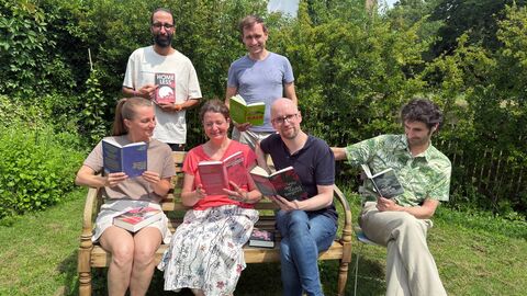 Mitarbeiter des Verlags Edition W sitzen lesend auf einer Bank.